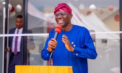 Smiling man in blue speaks at podium outdoors.