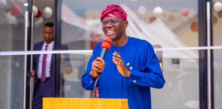 Smiling man in blue speaks at podium outdoors.