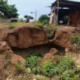 Eroded landscape with vegetation and nearby buildings.
