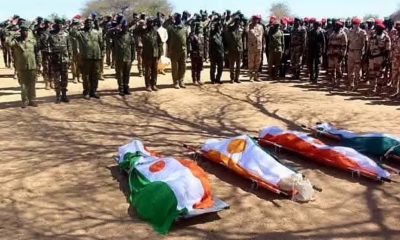 Soldiers saluting covered caskets at a military funeral.